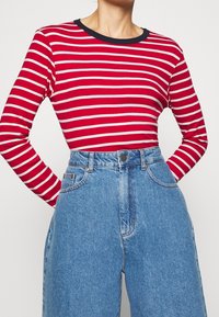 Langärmliges rot-weiß gestreiftes Shirt mit einem runden Ausschnitt in Marineblau, kombiniert mit hochtaillierten hellblauen Denim-Jeans mit Knopfverschluss.