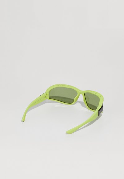 Gafas de sol verde claro con lentes verde oscuro, brazos curvados y acentos texturizados en la montura, con un diseño minimalista.
