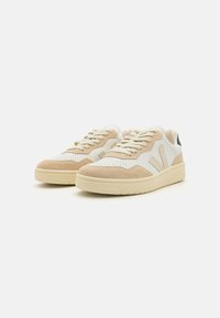 Beige-weiße Sneaker aus Wildleder und Leder, runde Zehenform, Schnürdesign, perforierte Details an der Zehenpartie und strukturierte Sohle.