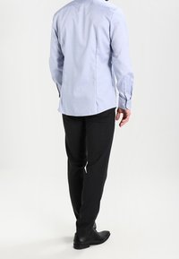 Ljusblå skjorta med knappar och långa ärmar, ryggveck och rundad nederkant, tillsammans med slim-fit svarta byxor och svarta skor.