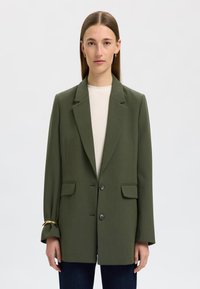 Olivenfarget blazer med avslappet passform, notched lapels, to frontlommer og to knapper. Har et gullakcent ved mansjetten.