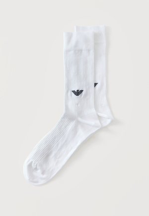 Paar weiße gerippte Knöchelsocken mit schwarzem Logo nahe dem Knöchel, flach auf hellem Hintergrund ausgelegt.