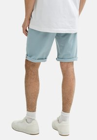 Shorts de un albastru deschis, cu margini ruliate, din material, purtate cu sneakerși albi și șosete albe. Focalizare pe picioare și vedere din spate, cu detalii minime.