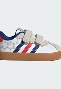 Zapatilla blanca para niño con rayas azules y rojas, tiras de velcro beige y suela de goma marrón.