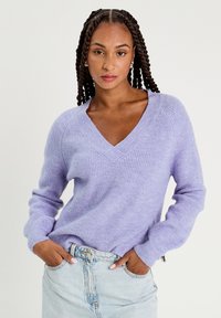 Paarse gebreide trui met een V-hals, lange mouwen en een geribbeld textuur, gecombineerd met een lichtblauwe jeansrok.