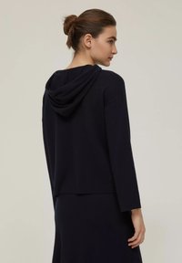 Felpa blu navy con maniche lunghe, orlo arrotondato e tessuto morbido. Caratterizzata da una vestibilità rilassata e un cappuccio con cordino. Texture liscia.