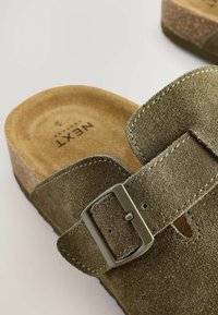 Green suede slip-on sandal with a cork footbed, featuring a silver buckle and contrasting stitching along the strap edge.