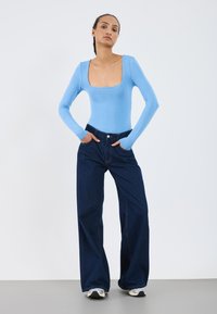 Lys blå langermet body med firkantet hals, kombinert med høy midje, vide mørk denim jeans. Glatt stofftextur.