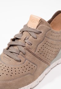 Bruna mockaskor med perforerade detaljer, grå snörning, en ljusbrun logotab och en fläckig vit sula. Designade för komfort och stil.