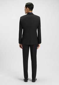 Completo nero con una vestibilità su misura, caratterizzato da spalle strutturate, maniche lunghe e pantaloni dritti. Il tessuto appare liscio con una leggera lucentezza.