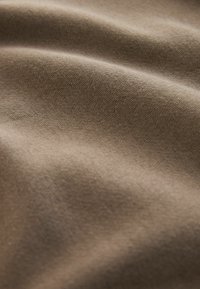 Tissu beige doux et lisse avec une texture fine en maille, présenté en doux plis et en gros plan.