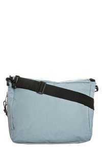 Bolso de hombro de tela azul claro con correa negra ajustable, forma rectangular, fondo plano y cierre de cremallera. Textura suave, diseño minimalista.