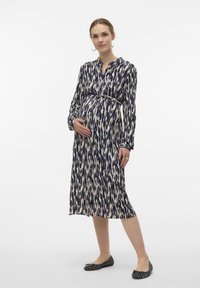 Lång, marinblå och krämfärgad mönstrad gravidklänning med krage, bälte i midjan och långa ärmar, kombinerad med svarta platta skor.