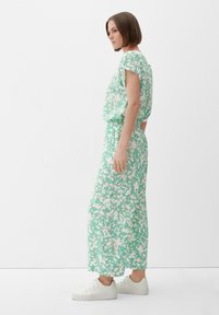 Maxi-jurk met bloemenpatroon in mintgroen en wit, met een relaxte pasvorm, korte mouwen en een elastische tailleband. Gecombineerd met witte sneakers.