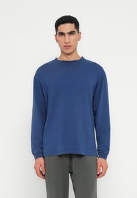 Dugoročnakusni plavi T-shirt s okruglim izrezom, izrađen od mekog materijala; ima ležeran kroj i minimalne detalje šivanja.
