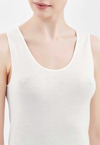 Top bianco senza maniche con scollatura a barca, realizzato in un tessuto liscio ed elastico. Presenta spalline sottili e un design aderente senza dettagli aggiuntivi.