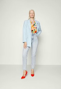 Blazer azul claro sobre uma blusa de padrão floral, combinado com jeans de denim claro de cintura alta e sapatos de salto agulha vermelhos. Design simples e ajustado.