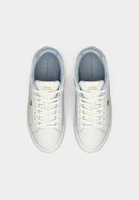 Un paio di sneaker bianche Tommy Hilfiger con lacci, interni imbottiti blu chiaro e piccolo logo sul lato, visto dall'alto su sfondo bianco.
