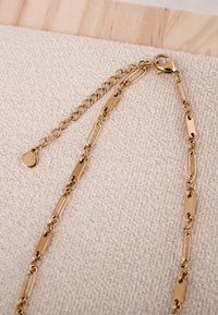 Zlatni lanac ogrlica s izduženim karikama, kopčom u obliku jastoga i podesivim produžnim lancem s malim okruglim privjeskom.