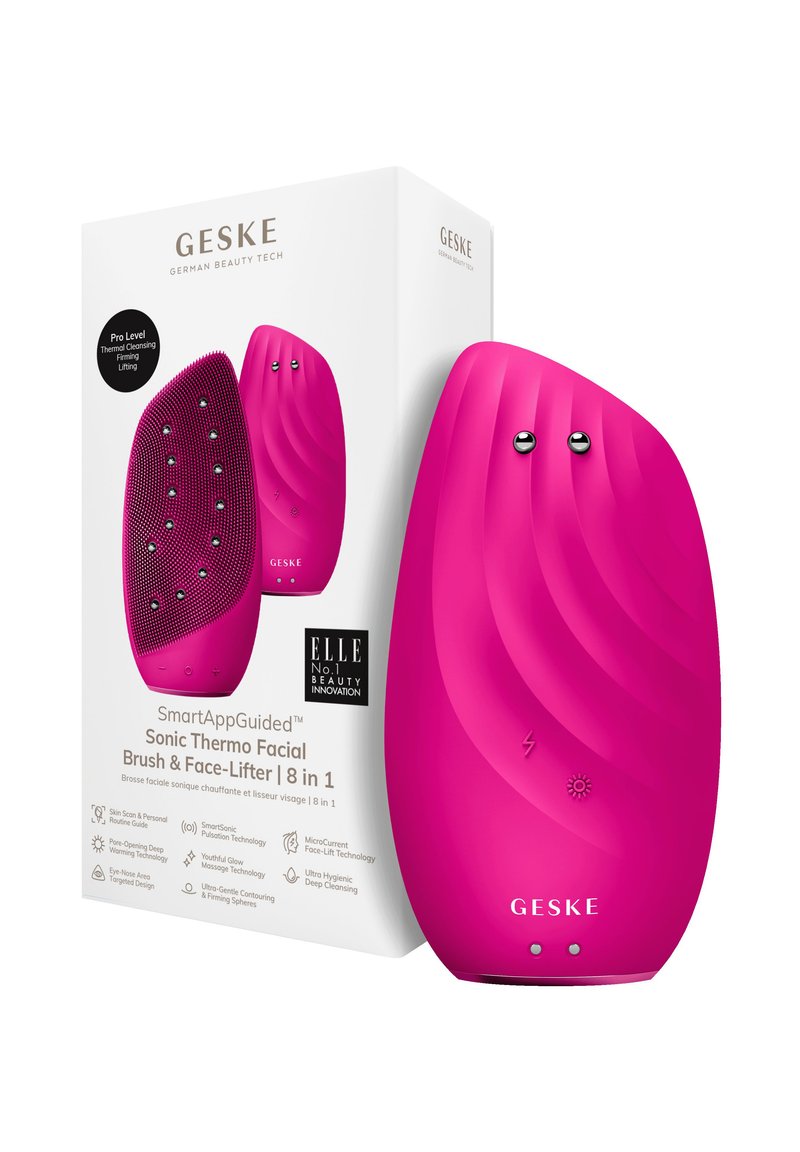 Brosse faciale en silicone rose avec texture nervurée, forme arrondie et accents argentés. La boîte présente les caractéristiques du produit et le branding.