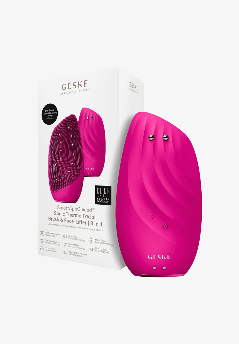Brosse faciale en silicone rose avec texture nervurée, forme arrondie et accents argentés. La boîte présente les caractéristiques du produit et le branding.