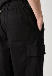 Svarte cargo-bukser med elastisk midje, sidelommer og en jevn tekstur, som fremhever praktiske designelementer og nytte.