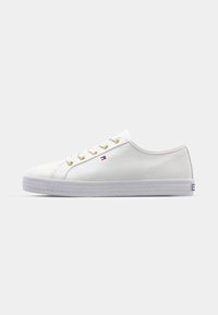 White low-top canvas sneaker with gold eyelets, white laces, and a small red, white, and blue flag logo on the side.