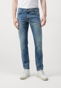 Lichtblauwe denim jeans met een slim fit, voorzien van vijf zakken, subtiele vervaging en een metalen knoopsluiting. Gepaard met witte sneakers.