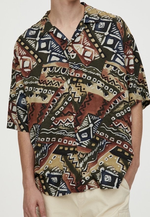 Camisa de botones de manga corta con un patrón tribal multicolor en tonos terrenales, con un corte relajado y una tela suave y texturizada.