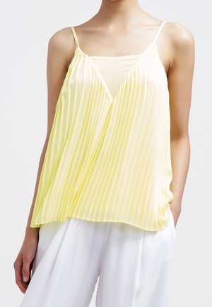 Mouwloze, lichtgele, geplooide cami met een V-hals over een bijpassende binnenlaag, gecombineerd met losse witte broek.