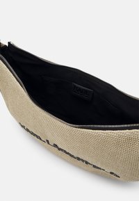Pochette beige tissée avec fermeture éclair, doublure intérieure noire et une petite poche intérieure étiquetée à la marque.