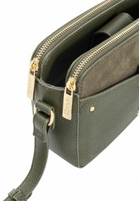 Ciemnozielona torebka skórzana typu crossbody o teksturowanej powierzchni, z dwiema złotymi zamkami błyskawicznymi, zamszową przednią kieszenią i regulowanym paskiem.