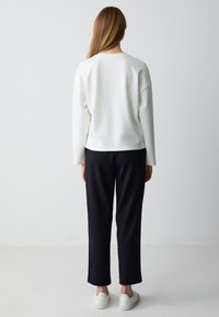Felpa bianca con scollatura rotonda e spalle abbassate, abbinata a pantaloni neri dalla vestibilità comoda e scarpe da ginnastica bianche. Design semplice e moderno.