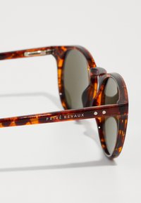 Brown tortoiseshell sunglasses with round lenses, metal accents, and branding along the temple. Lens color is dark gray.