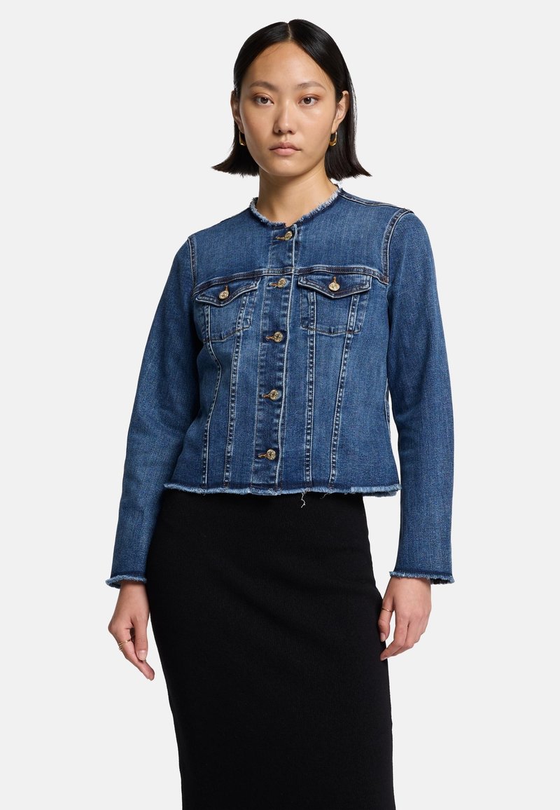 Jeansjacke mit goldenen Knöpfen, zwei Brusttaschen, fransigem Saum und blauer Waschung. Lange Ärmel und taillierte Passform, kombiniert mit einem schwarzen Rock.