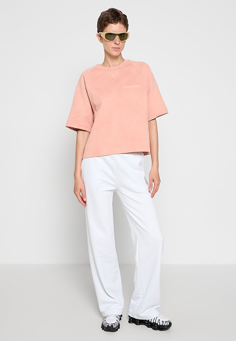 Jasnoróżowy, oversize t-shirt z kieszenią na piersi, zestawiony z luźnymi, białymi spodniami i butami w czarno-białe wzory.