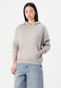 Haut à capuche gris clair avec une poche kangourou à l'avant, des poignets côtelés, et une coupe décontractée. Associé à un jean en denim bleu clair.