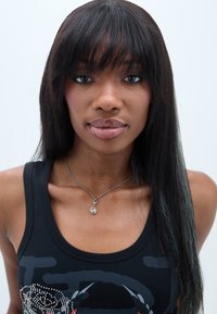 Svart tanktop med grafisk design; langt rett mørkt hår; sølvsmykke med en liten amulett; nøytral bakgrunn.