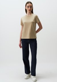 T-shirt beige a maniche corte con scollatura rotonda, abbinato a jeans a gamba dritta blu scuro e sneaker bianche. Design semplice e aderente.