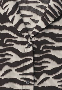 Gros plan d'une chemise à rayures zèbre noire et blanche avec un col pointu et deux boutons noirs visibles.