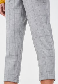 Pantalons gris à carreaux en tissu texturé, avec un motif à damier et des ourlets retroussés. Coupe ajustée avec un design à jambes droites.
