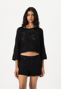 Zwart cropped trui met bloemen uitsnijdingen en klokmouwen, gecombineerd met zwarte denim shorts. Soepele textuur, casual ontwerp.