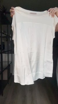 White short-sleeve top made of smooth fabric, features a rounded neckline and an asymmetric hem, with a partially sheer overlay at the front.