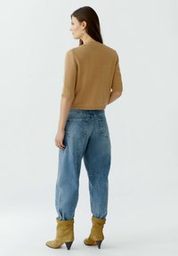 Beige gestrickter Kurzarm-Pullover mit Rippenbündchen, kombiniert mit lockeren blauen Denim-Jeans und gelben Knöchelstiefeln mit spitzer Zehenform.