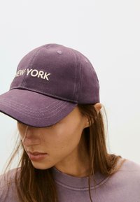 Lila bomullsmössa med broderad "NEW YORK" i krämfärg. Har en böjd skärm och sexpaneldesign, lämplig för avslappnad användning.