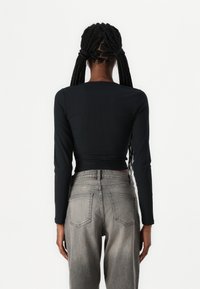 Μαύρο μακρυμάνικο cropped τοπ συνδυασμένο με ψηλόμεσα γκρι τζιν. Το τοπ διαθέτει ριγωτή υφή ενώ τα τζιν έχουν πίσω τσέπες.