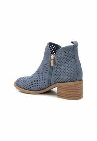 Stivale alla caviglia blu in suede con zip laterale e tacco in legno impilato. Texture liscia con fori circolari in tutto il pannello.