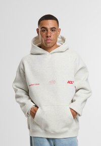 Světle šedá mikina s kapucí vyrobená z bavlněné směsi, s červeně potištěnými logy "Another Cotton" a "ACL." Má volný střih a přední kapsy.