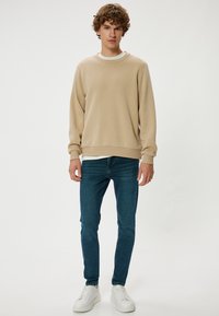 Harmaa puuvillaneule, jossa on pyöreä kaula-aukko, yhdistettynä sinisiin slim fit -farkkuihin ja valkoisiin tennareihin. Pehmeä pinta ja rento muotoilu.