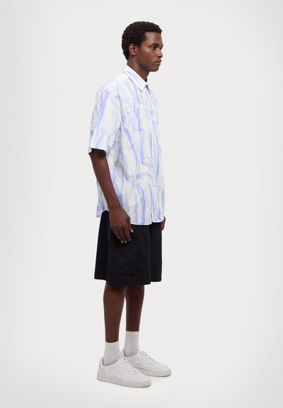 Kurzarm, knöpfbares Shirt mit einem blau-weißen Marmor-Muster; kombiniert mit schwarzen Shorts und weißen Sneakers. Glatter Stoff, lockere Passform.